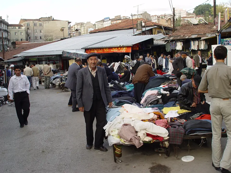 Ankara'da açık pazar yerinde tezgâhlar arasında yürüyen alışverişçiler, arkada tenteli giyim tezgâhları