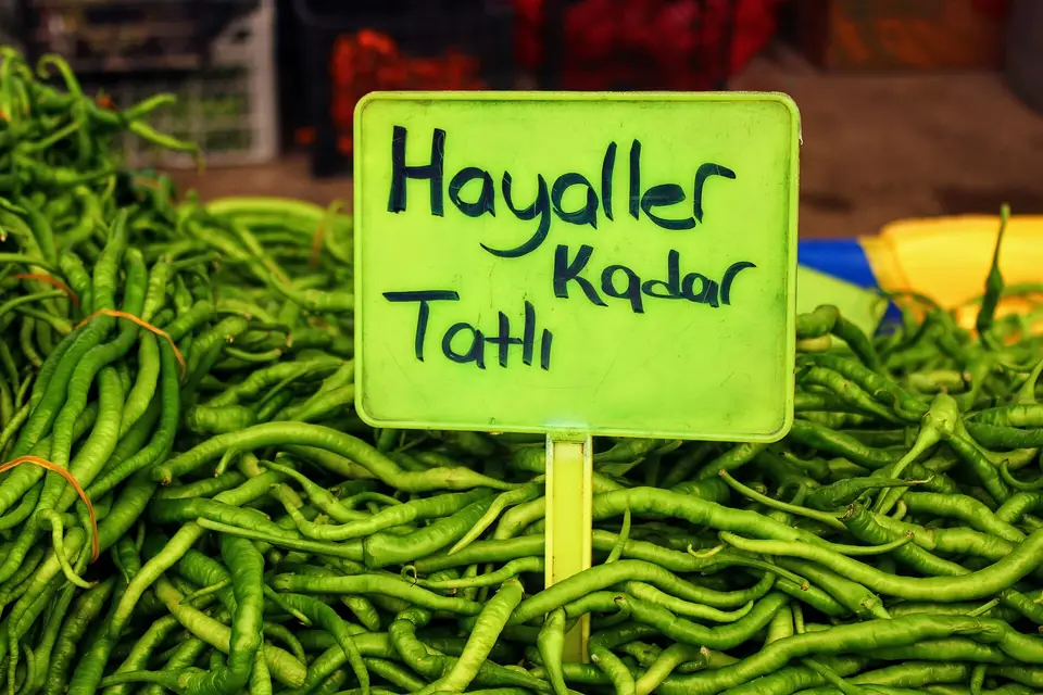 Pazar tezgâhında yığılmış sivri biberlerin üzerinde 'Hayaller Kadar Tatlı' yazan yeşil tabela