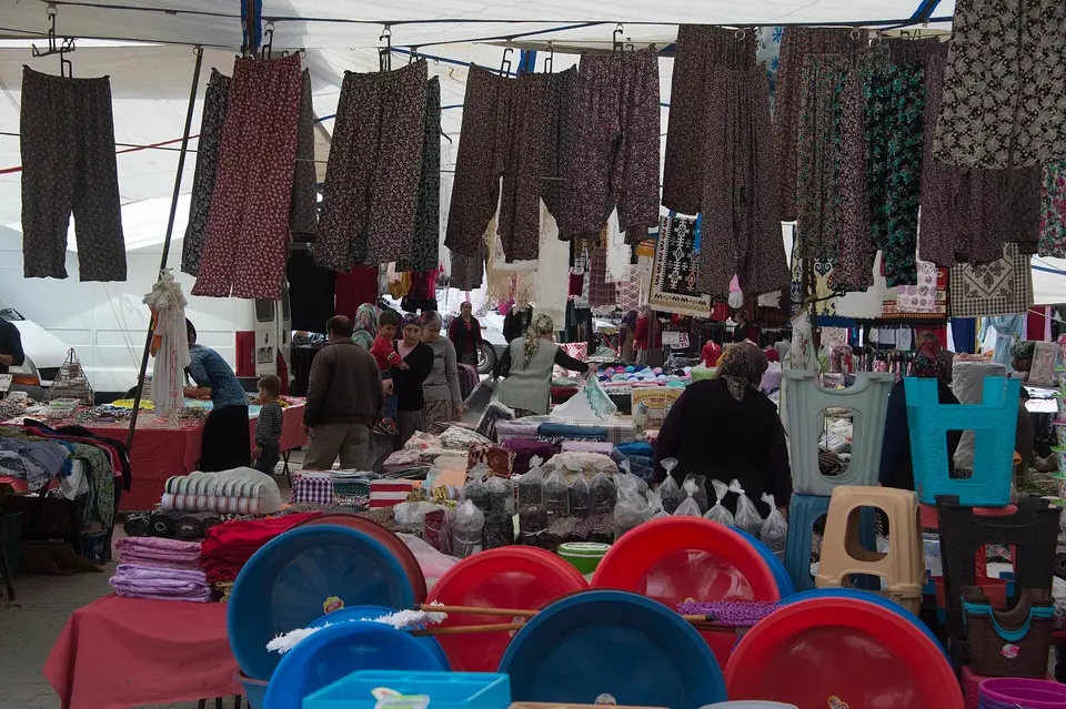 Kaş Kınık'ta pazar günü tezgâhlar arasındaki koridorda asılı giysiler ve plastik leğenler